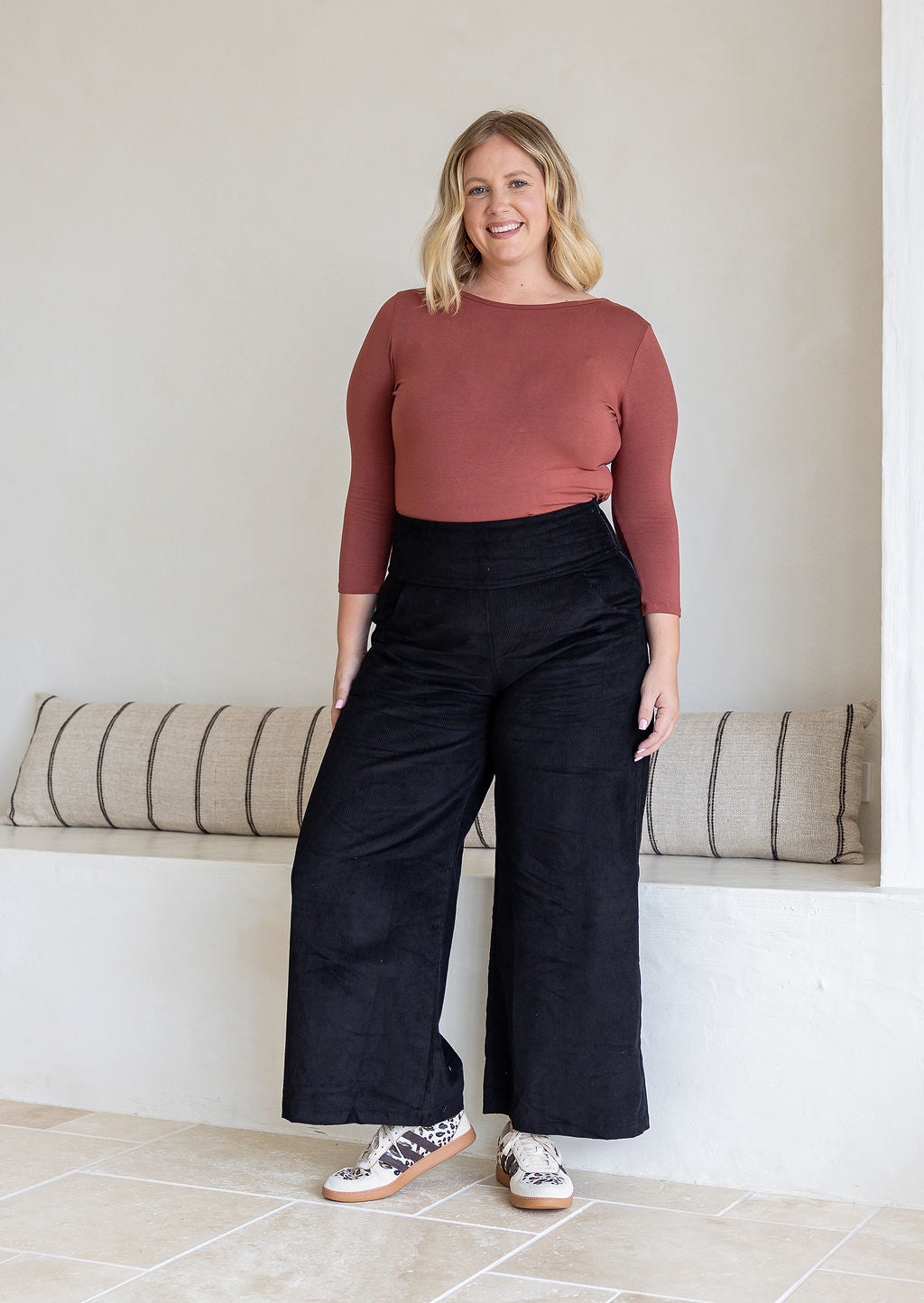Woman standing wearing black cotton corduroy wide leg pants and a dusty pink top