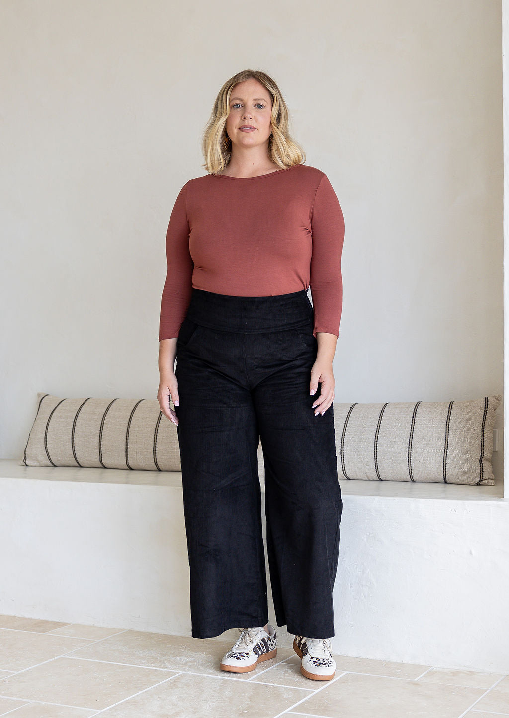 Woman wearing black cotton corduroy wide leg pants and a dusty pink top. 