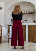 Woman stands backwards wearing a cotton corduroy wide leg pants in deep red with wide waistband and a side zip