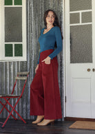 Woman in a red corduroy pants standing in a room with a red chair and white door.