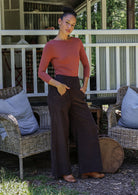 Woman standing on a porch wearing a pink top and brown pants.