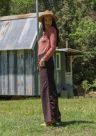 Woman in a pink top and brown corduroy pants standing in front of a rustic cabin.