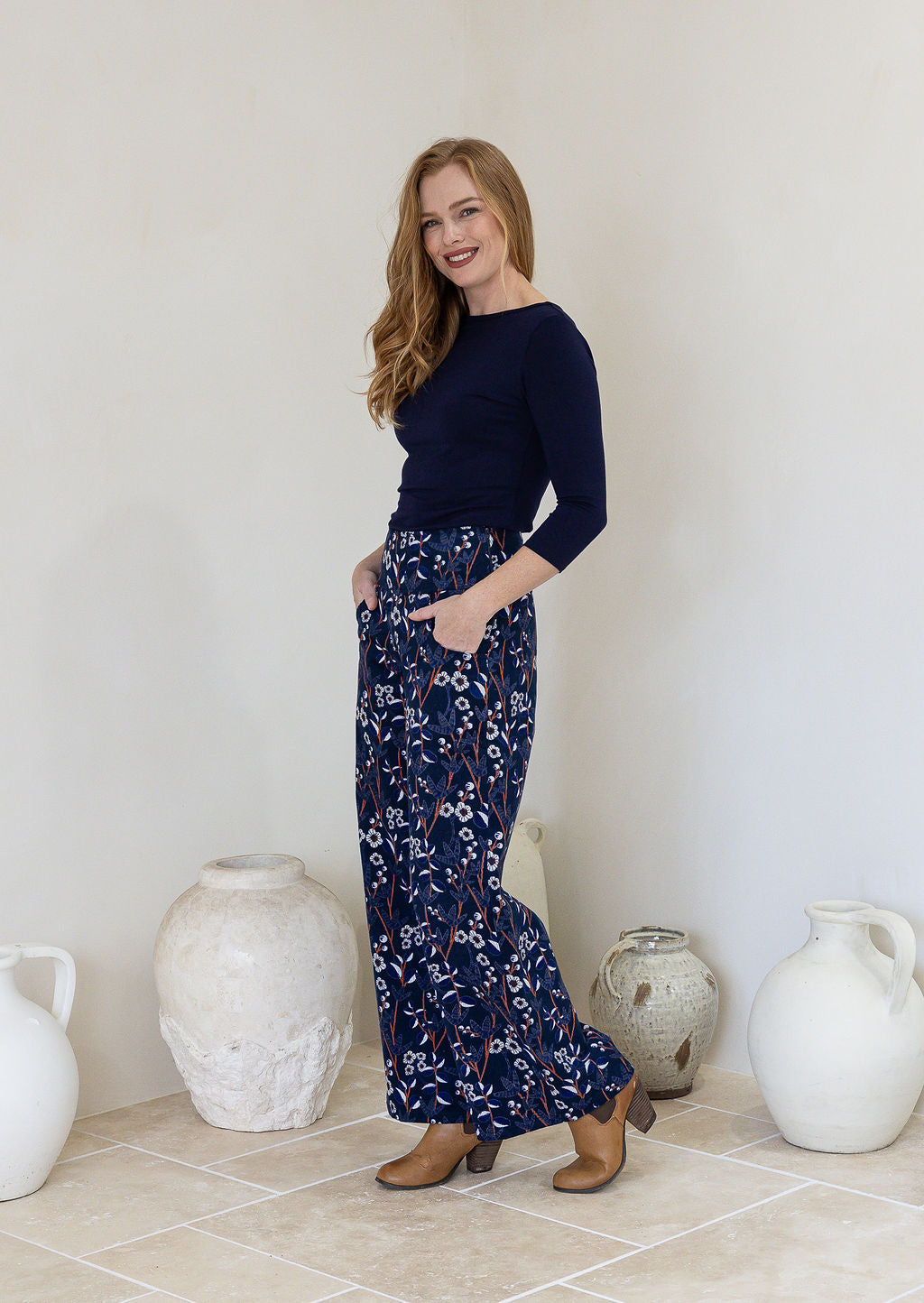 Woman stands sideways wearing a wide leg cotton corduroy pants in navy blue based floral print.