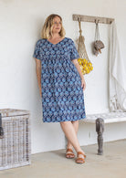 Model wearing a cotton V-neck short sleeve dress in blue based floral print with empire waistline and  pocket.
