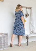 Model stands backwards wearing a cotton V-neck relaxed fit dress with empire waistline and short sleeves.