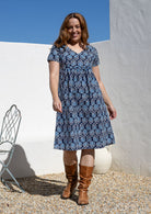 Model wearing a cotton V-neck short sleeve dress in blue based floral print with empire waistline and  pocket.