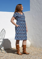 A woman wearing a blue and white floral short-sleeve dress with brown boots, standing outdoors. 
