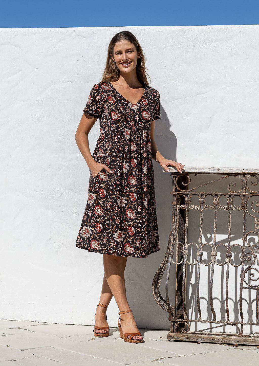 Model wearing a cotton knee length dress with empire waist, short sleeves and one hand in pocket.