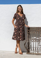 Model wearing a cotton knee length dress with empire waist, short sleeves and one hand in pocket.
