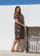 Model stands sideways wearing a cotton V-neck relaxed fit dress with empire waistline and short sleeves.