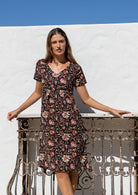 Woman wearing a 100% cotton black based floral print dress with V neckline and short sleeves.