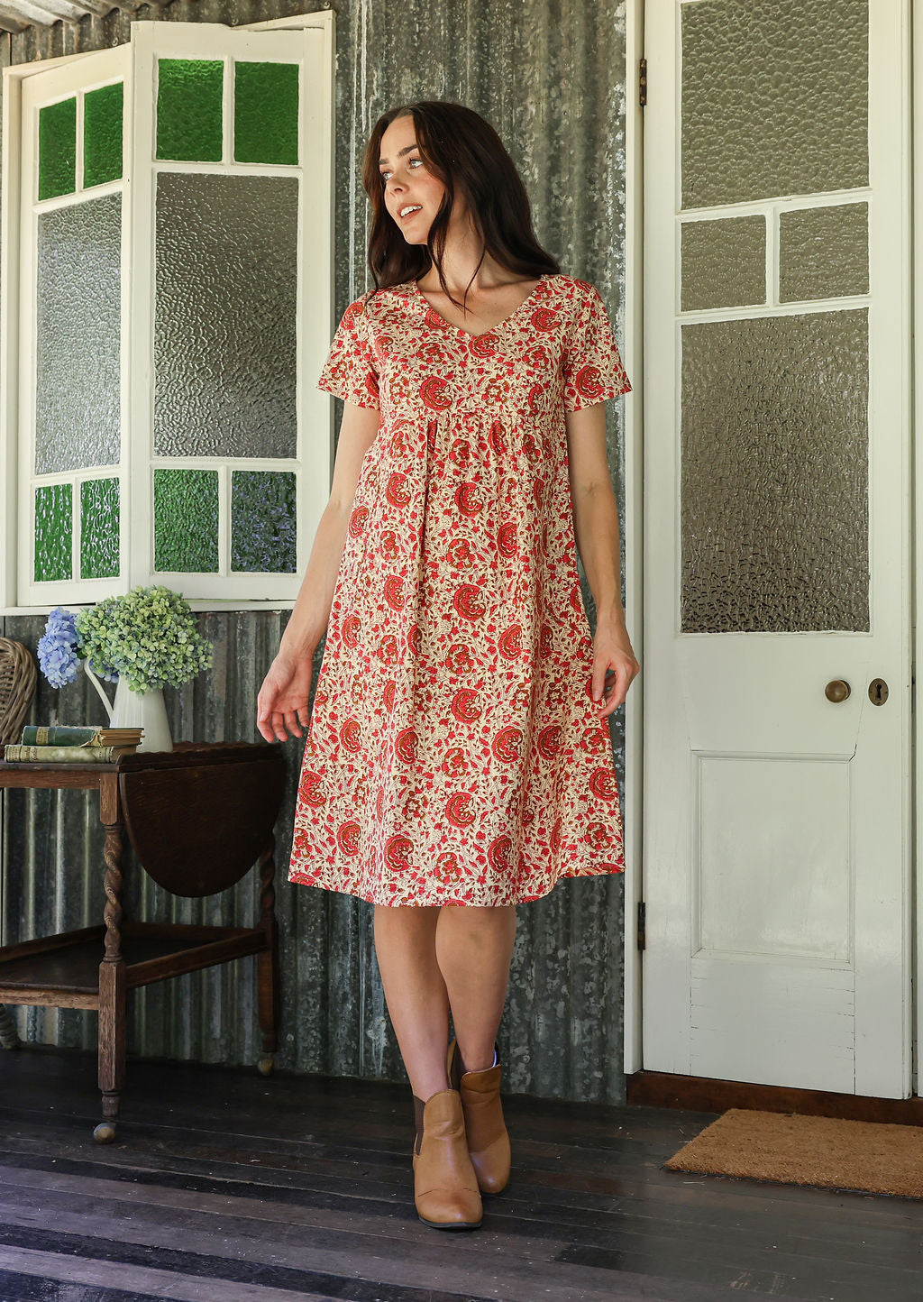 Woman in a floral dress standing in a room with patterned walls and a door.