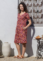 Model stands sideways wearing a cotton V-neck relaxed fit dress with empire waistline and short sleeves.