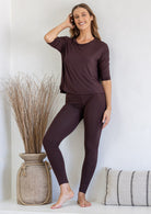 Woman wearing a dark brown rayon jersey relaxed fit top with fitted 3/4 sleeves, paired with dark brown leggings