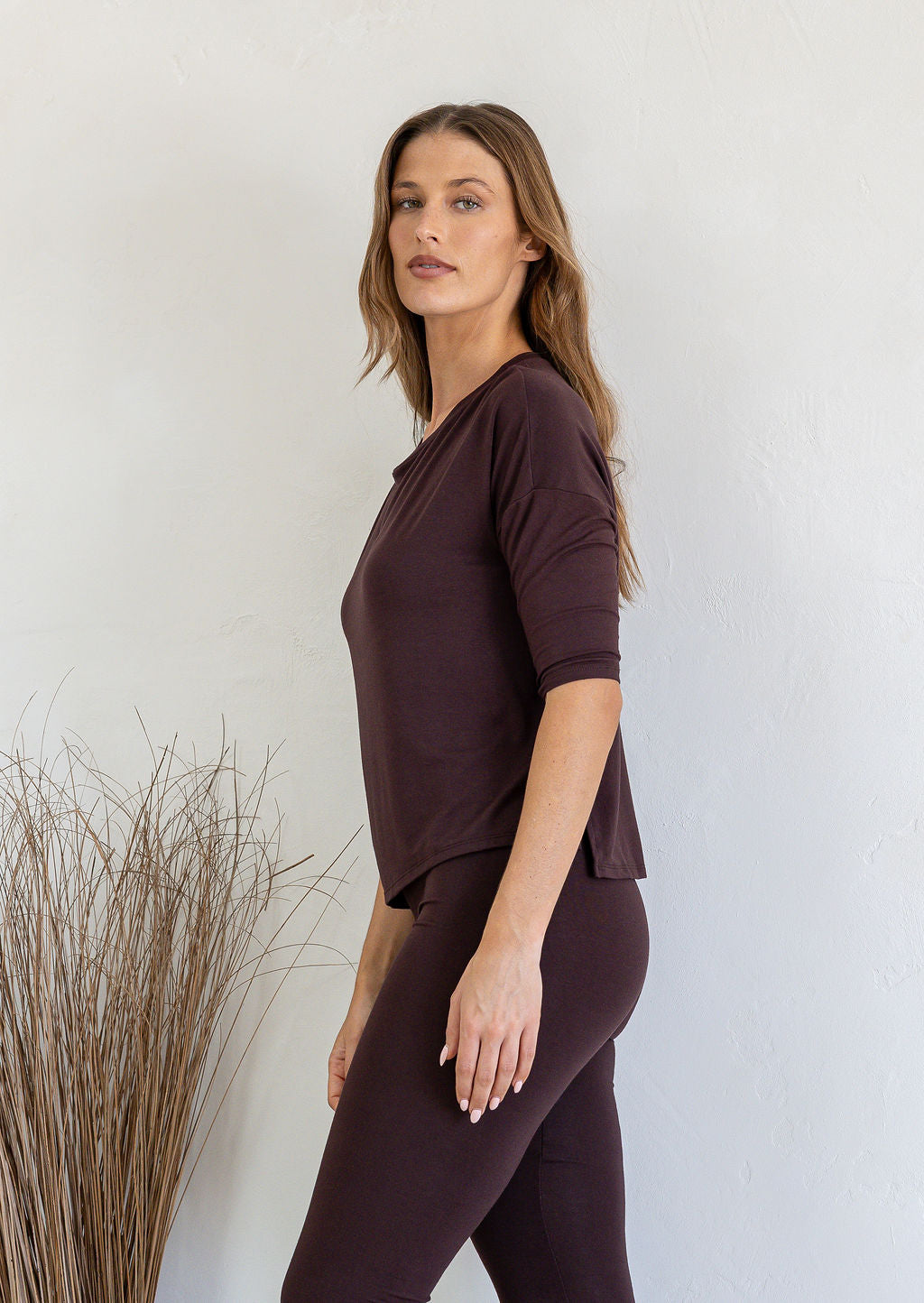 Woman wearing a brown rayon jersey outfit standing against a white wall with decorative elements