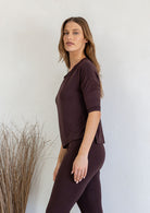 Woman wearing a brown rayon jersey outfit standing against a white wall with decorative elements