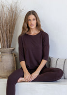 Woman wearing a dark brown rayon jersey relaxed fit top with a drop shoulder, round neckline and fitted 3/4 sleeves, paired with leggings