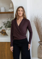 Woman wearing a false wrap front, long sleeve top in dark brown stretch rayon jersey, in a light filled room