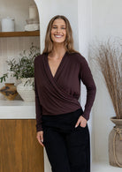 Woman smiles wearing a false wrap front, long sleeve top in dark brown stretch rayon jersey with a deep V-neckline