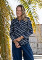 Woman wearing a navy floral cotton top and navy plain pants standing in front of palm leaves.