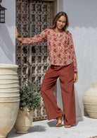 Woman in a 100% cotton top and red pants standing in front of a decorative wooden door.