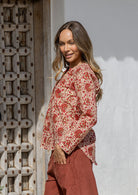 Woman standing sideways wearing a 100% cotton full sleeves top in cream based floral print with V neckline