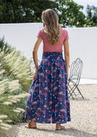 Woman standing backwards wearing a pink top and wide legged navy blue cotton floral pants. 