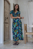A woman modeling a short-sleeve wrap maxi dress with a navy blue based multicolour floral print. 
