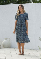 Woman wearing a 100% cotton blue floral dress standing against a white wall.