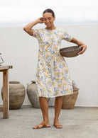 Woman in a 100% cotton floral dress holding a woven basket in an outdoor setting.