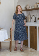 Woman wearing a navy blue based floral print cotton dress with one hand in pocket
