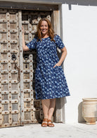 Woman wearing a navy blue based floral print cotton dress with one hand in pocket
