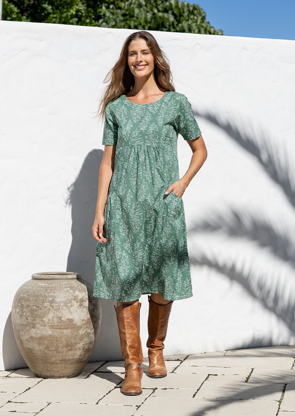 Woman wearing a sage green based floral print cotton dress with one hand in pocket
