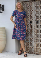 Woman wearing a relaxed fit blue floral cotton dress with round neckline, short sleeves and pockets with pin tucks.