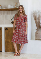 Woman wearing a red floral dress standing in a kitchen.