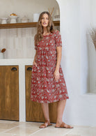 Woman wearing a red based floral print cotton dress with one hand in pocket