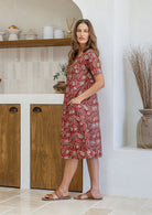 Woman stands sideways wearing a 100% cotton dress in red based floral print with short sleeves