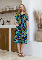 Woman poses in a navy based cotton colourful floral short sleeve dress with round neckline