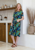 woman wearing a 100% cotton dress with one hand in pocket in navy based colourful florals