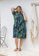 Woman poses in a navy based cotton colourful floral short sleeve dress with round neckline