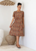 Woman wearing a patterned floral cotton dress standing in a room with a couch and decorative items.