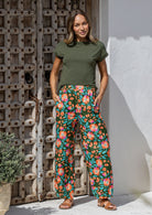Woman wearing a basic top and wide leg cotton pants in olive green based floral print with both hand in pockets.
