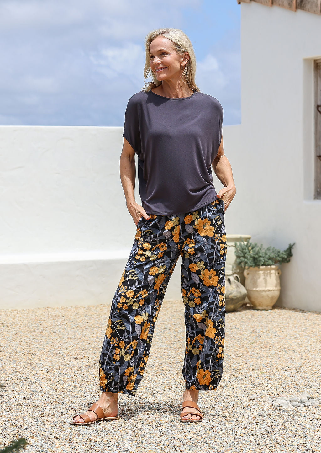 Woman wearing a dark gray top and floral pants cotton pants with pockets, elastic waits and pleated ankles 