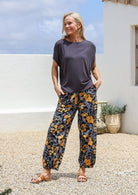 Woman wearing a dark gray top and floral pants cotton pants with pockets, elastic waits and pleated ankles 
