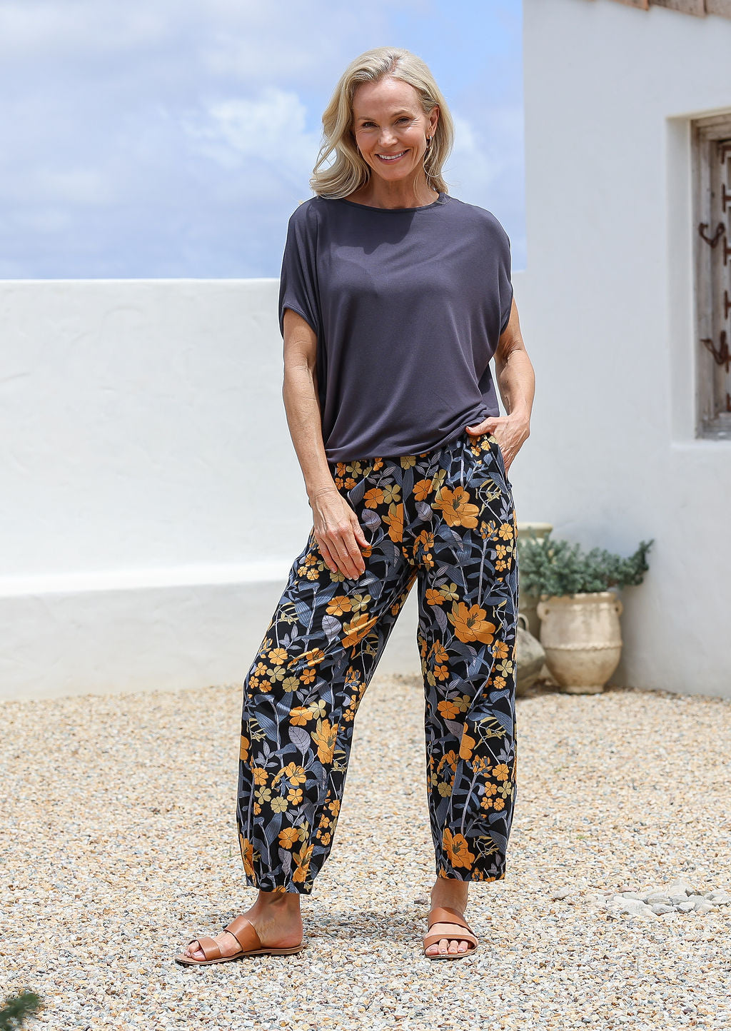 Model stands with a hand in pocket wearing a 100% cotton wide leg pant in retro floral print on black base