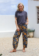 Model stands with a hand in pocket wearing a 100% cotton wide leg pant in retro floral print on black base