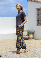Model stands sideways with one hand in pocket wearing relaxed-fit tapered cotton pants with pleats at the ankles and an elastic waistband.