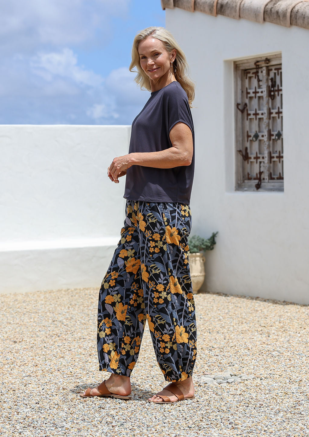Woman wearing a dark basic top and floral  cotton wide-leg pants with elastic waist and pleated ankles in black based yellow and grey floral print