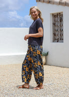Woman wearing a dark basic top and floral  cotton wide-leg pants with elastic waist and pleated ankles in black based yellow and grey floral print