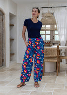 Woman standing wears 100% cotton wide leg floral print pants in royal blue based with elastic waist, pockets and pleated ankles